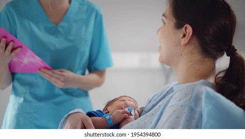 Happy mother holding newborn baby talking to doctor in hospital. Portrait of young woman holding infant son lying in hospital bed and listening to nurse in clinic