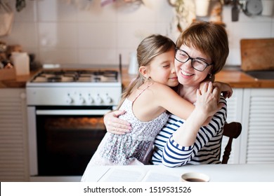 Happy Mother Is Hugging Daughter In Cozy Home Kitchen. Woman And Cute Child Girl Are Smiling. Family Is Using Oven. Kid Is Enjoying Kindness, Embrace, Care, Support. Lifestyle Authentic Moment.