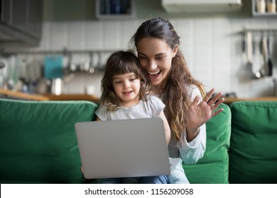 Happy mother and kid daughter waving hands looking at web camera using laptop for video call, smiling mom and child girl having fun greeting online by computer webcam making videocall via application