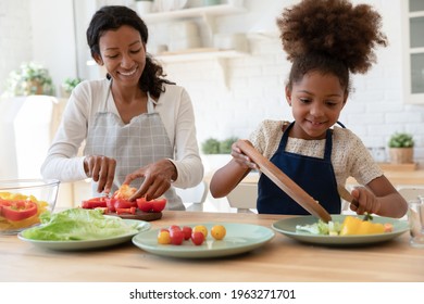Happy mother and kid sharing cooking chores, preparing salad for dinner together, slicing fresh vegetables on chopping boards, talking and laughing. Family eating at home, healthy food concept - Shutterstock ID 1963271701
