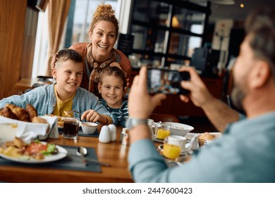 Happy mother with kids being photographed during family breakfast in a hotel. - Powered by Shutterstock