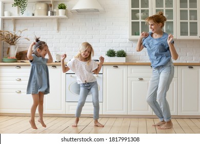 Happy Mother And Kids Dancing And Frolicking Barefoot On Wooden Floor In Cozy Spacious Kitchen. Young Mom And Preschool Daughters In Casual Clothes Spending Time At Home Having Fun Together