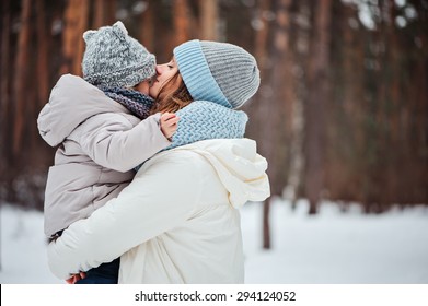 Happy Mother Kissing Baby Girl On The Walk In Winter Snowy Forest 