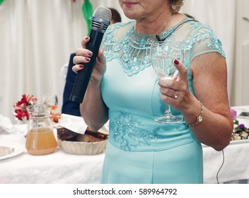 Happy Mother In Law With Champagne In Glass Holding Microphone And Pronouncing Toast At Wedding Reception Of Her Daughter In Restaurant