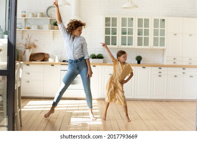 Happy mother and little daughter moving to favorite music in modern kitchen together, young mom teaching adorable kid girl to dance, family engaged in funny activity at home, enjoying leisure time