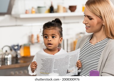 Happy Mother Looking At Adopted African American Kid With Newspaper