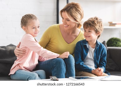happy mother looking at adorable smiling children sitting together on couch  - Shutterstock ID 1272166543