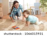Happy mother looking at her baby son crawling on floor in children room