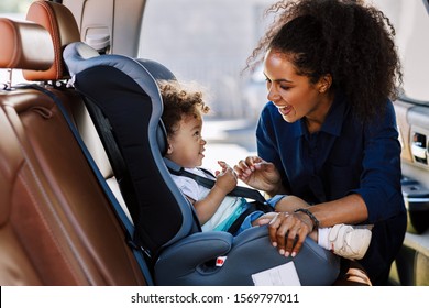 Happy mother looking at her son in a baby seat. Young female preparing kid for a trip.