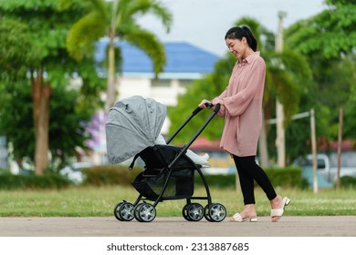 happy mother looking and pushing infant baby stroller while walking in the park