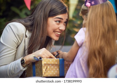 Happy Mother Opening Birthday Gift With Her Cute Child Girl.