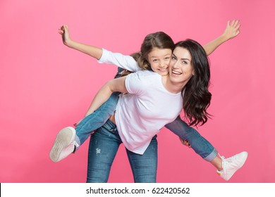 Feliz madre piggyback adorable pequeña hija sonriendo a la cámara Foto de stock