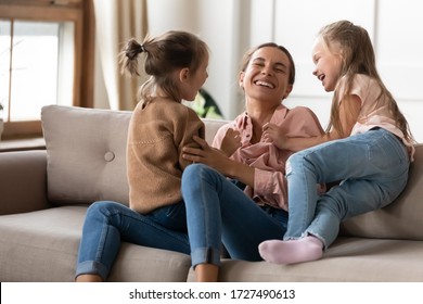 Happy Mother Playing With Two Little Daughters, Sitting On Couch At Home, Cute Preschool Girls Tickling Laughing Mum, Family Having Fun, Spending Weekend Together, Playing Funny Game