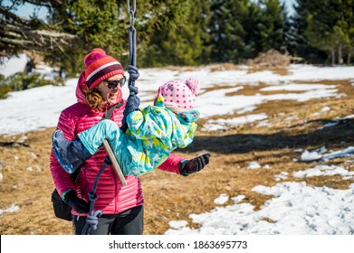 Happy mother protecting her daughter while she swings outdoor.