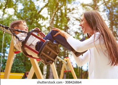 happy mother pushing laughing son on swing in a park - Shutterstock ID 308426864