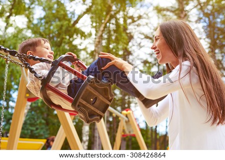 happy mother pushing laughing son on swing in a park