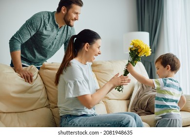 Happy Mother Receiving Bouquet Of Yellow Flowers From Her Son At Home. 