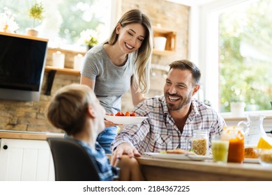 Happy mother serving food to her family while father and son having fun in dining room - Powered by Shutterstock