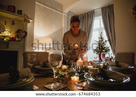 Happy mother is setting the table for Christmas dinner with her family.  She is lighting candles.