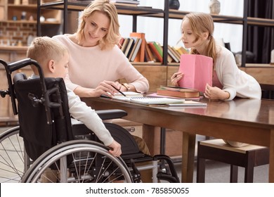 happy mother showing something in book to son on wheelchair