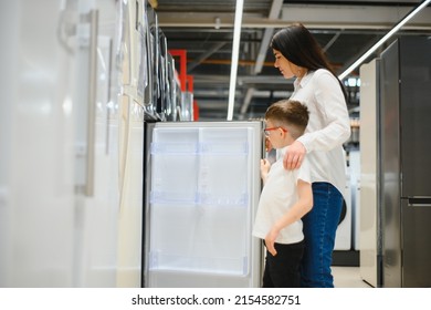 Happy Mother With Son Choosing Refrigerator In Home Appliance Store.