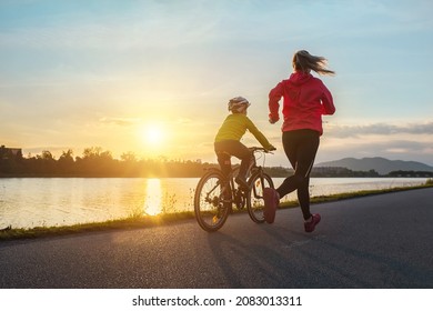 Happy mother and son go in sports outdoors. Boy rides bike in helmets, mom runs on sunny day. Silhouette family at sunset. Fresh air. Health care, authenticity, sense of balance and calmness