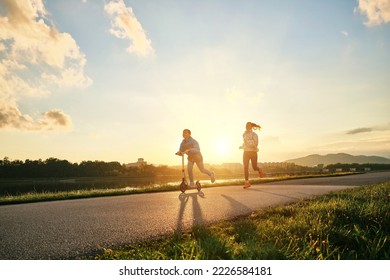 Happy mother and son go in sports outdoors. Boy rides scooter, mom runs on sunny day. Silhouette family at sunset. Fresh air. Health care, authenticity, sense of balance and calmness.