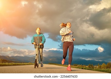 Happy mother and son go in sports outdoors. Boy rides scooter, mom runs on sunny day. Silhouette family at sunset. Health care, authenticity, sense of balance and calmness. - Shutterstock ID 2256607633