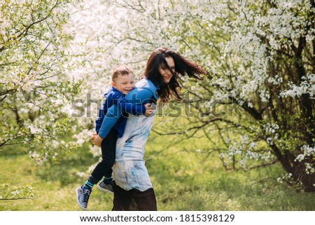 Happy mother and son play and have a fun on sunlit glade against background of blooming spring garden.