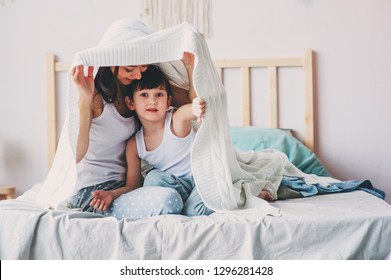 Happy Mother And Son Playing And Hiding Under Blanket In Bed In Cozy Weekend Morning. Casual Lifestyle With Real Family