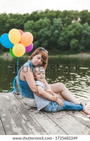 Happy mother and son are sitting in the evening at sunset on a pier near the river. Mother's day concept.
