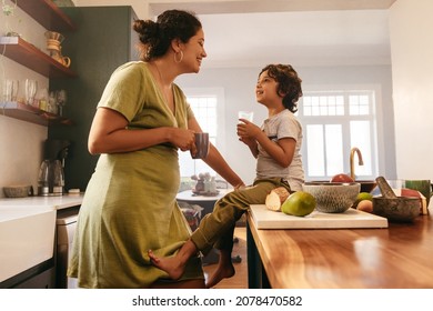 Happy mother and son smiling at each other affectionately. Mother and son drinking their morning beverages in the kitchen at home. Caring single mother bonding with her young son. - Shutterstock ID 2078470582
