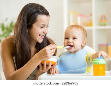 Happy Mother Spoon Feeding Baby Child At Home