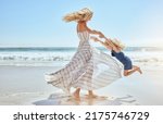 Happy mother swinging and spinning cute daughter in circles by the arms at the beach. Playful, energetic and joyful kid having fun while bonding with mom on sunny summer vacation outdoors