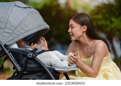 happy mother talking and playing with her infant baby in the stroller while resting in the park