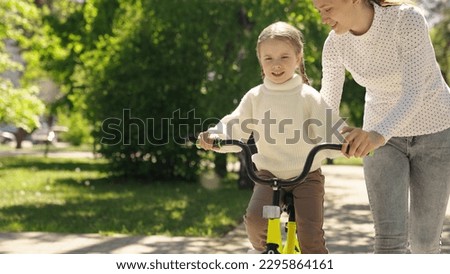 happy mother teaches little Child ride bicycle. Little daughter girl dreams traveling by bike. Walk park. Happy family. Kid rides his bike through park for first time. Mom Child Bike. drive bicycle