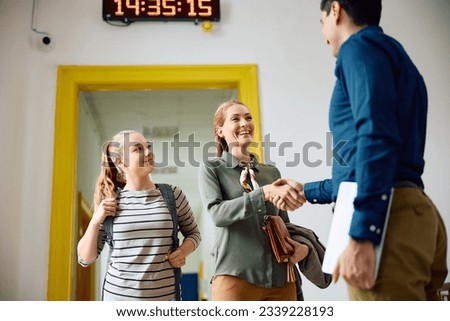 Happy mother with teenage daughter greeting high school principal in a hallway. 