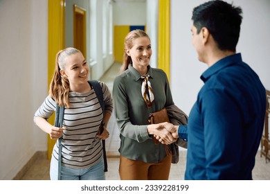 Happy mother of teenage girl shaking hands with high school principal in a hallway.