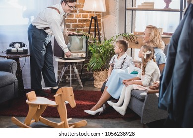 happy mother with two children looking at father turning on vintage tv, 50s style