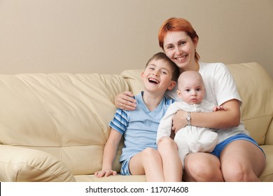 Happy Mother With Two Children Sits On A Sofa.