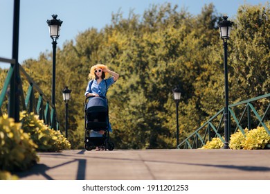 Happy Mother Walking Baby Outdoors In Stroller. Stylish Tourist Mom Spending Family Vacation With Her Child
