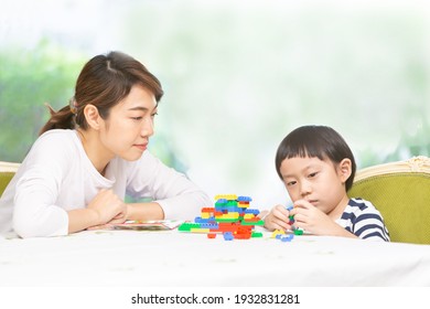 Happy Mother Watching Her Son Play On The Table Beside A Gardent, Home School And Learning By Playing Education Concept