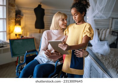 Happy mother in wheelchair with child using digital tablet at home. People family happiness concept. - Powered by Shutterstock