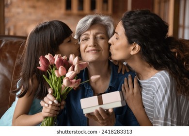 Happy Mothers Day. Affectionate young adult woman daughter and little kid girl granddaughter greeting excited mature latin lady mommy grandmother with birthday holiday kiss give flowers present gift - Powered by Shutterstock