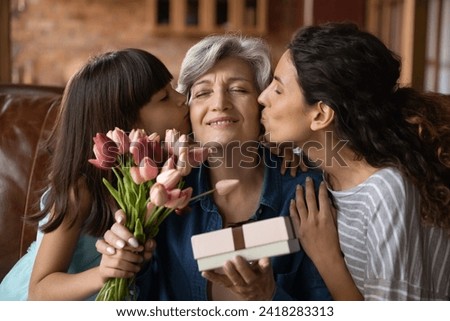 Happy Mothers Day. Affectionate young adult woman daughter and little kid girl granddaughter greeting excited mature latin lady mommy grandmother with birthday holiday kiss give flowers present gift