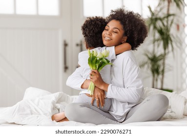 Happy mother's day! Afro american family happy baby daughter congratulates mom on the holiday, hugs her and gives bouquet of flowers at home - Powered by Shutterstock