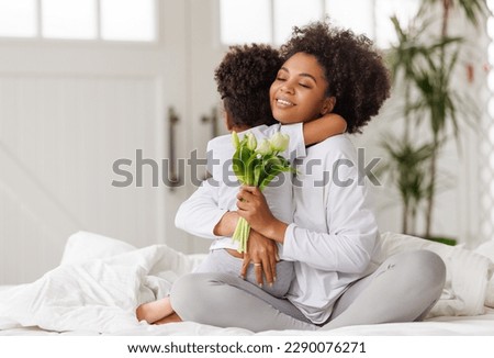 Happy mother's day! Afro american family happy baby daughter congratulates mom on the holiday, hugs her and gives bouquet of flowers at home Foto stock © 
