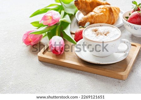 Happy mother's day, beautiful breakfast, lunch with cup of coffee (cappuccino) fresh croissants, strawberries on tray, bouquet of tulips as gift. Festive concept. Spring holiday, family relations.