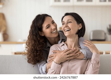 Happy Mothers Day celebration, family ties and unconditional love. Cheerful beautiful grown up millennial daughter cuddling from behind her lovely mature mother, express care, support and affection - Powered by Shutterstock