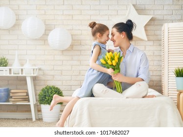 Happy mother's day! Child daughter is congratulating mom and giving her flowers tulips. Mum and girl smiling and hugging. Family holiday and togetherness. - Powered by Shutterstock